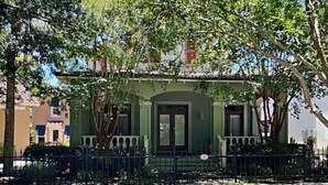 Une maison verte avec un porche et une clôture noire.
