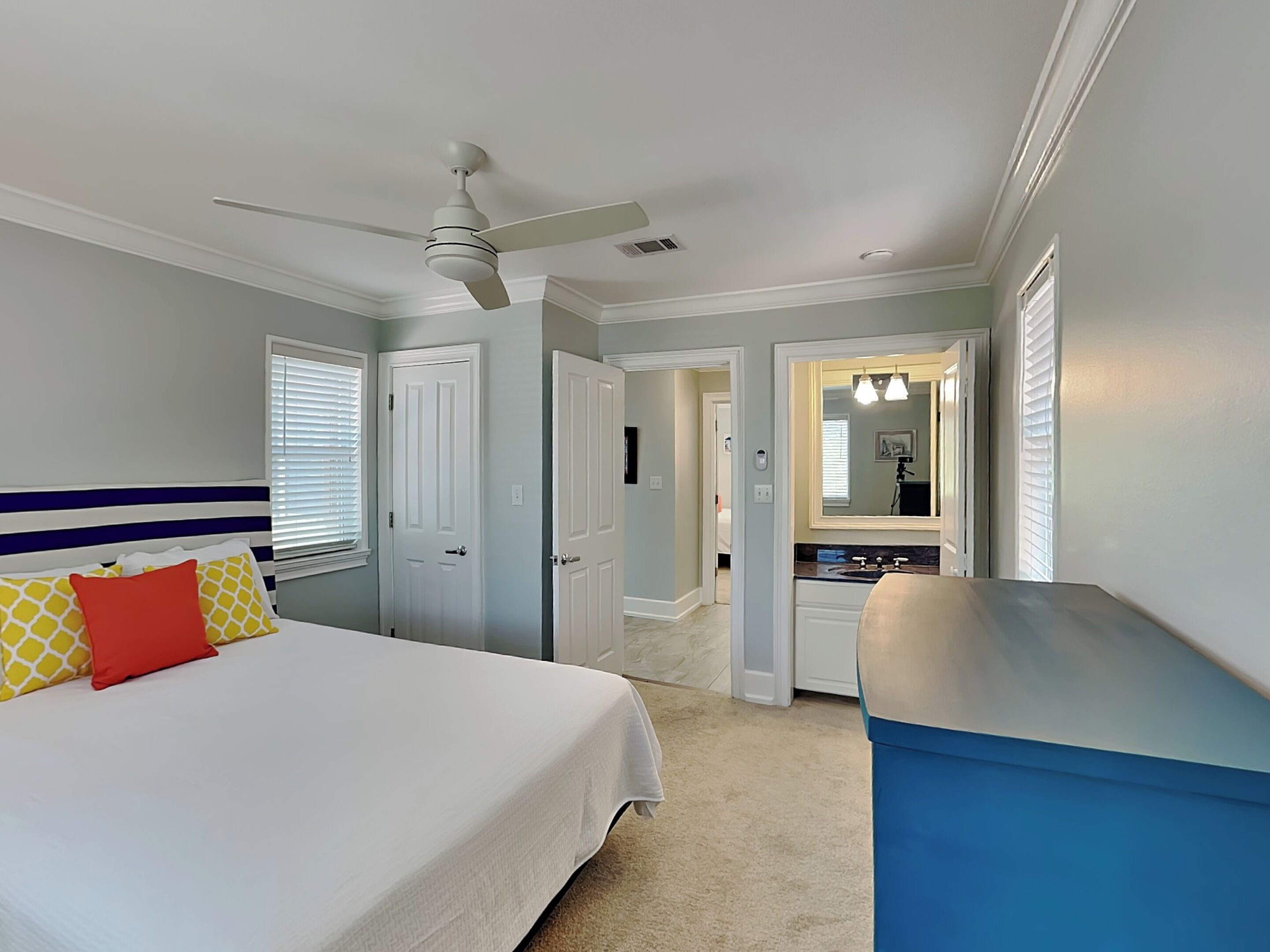 A bedroom with a bed, a ceiling fan, a bathroom with a sink and mirror, and a hallway leading to another room.