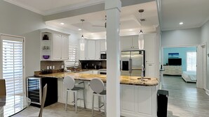 Une cuisine moderne avec des meubles blancs, un comptoir en granit et des appareils en acier inoxydable. On y trouve trois tabourets de bar et une table à manger en verre.