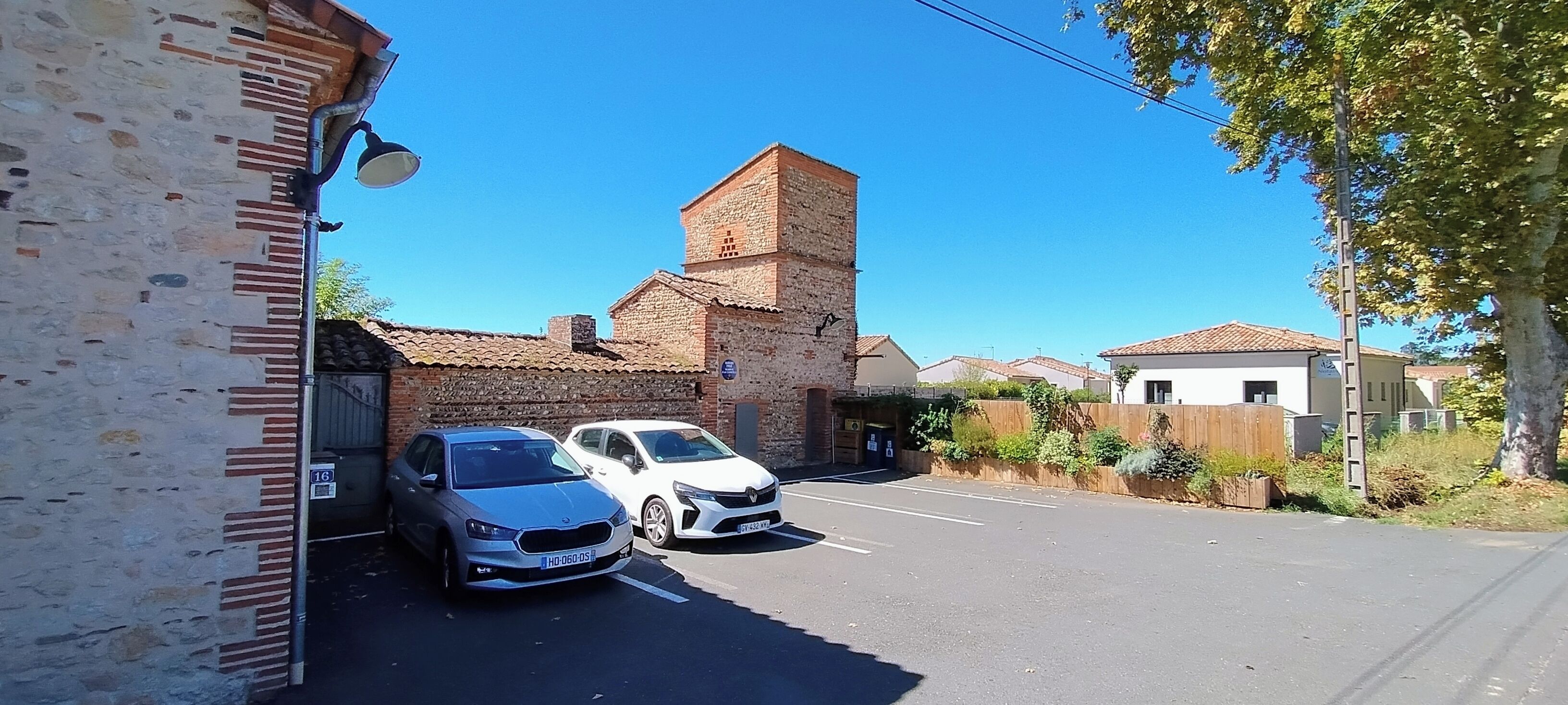 Un estacionamiento con dos coches, un edificio de ladrillo y un cielo azul despejado.