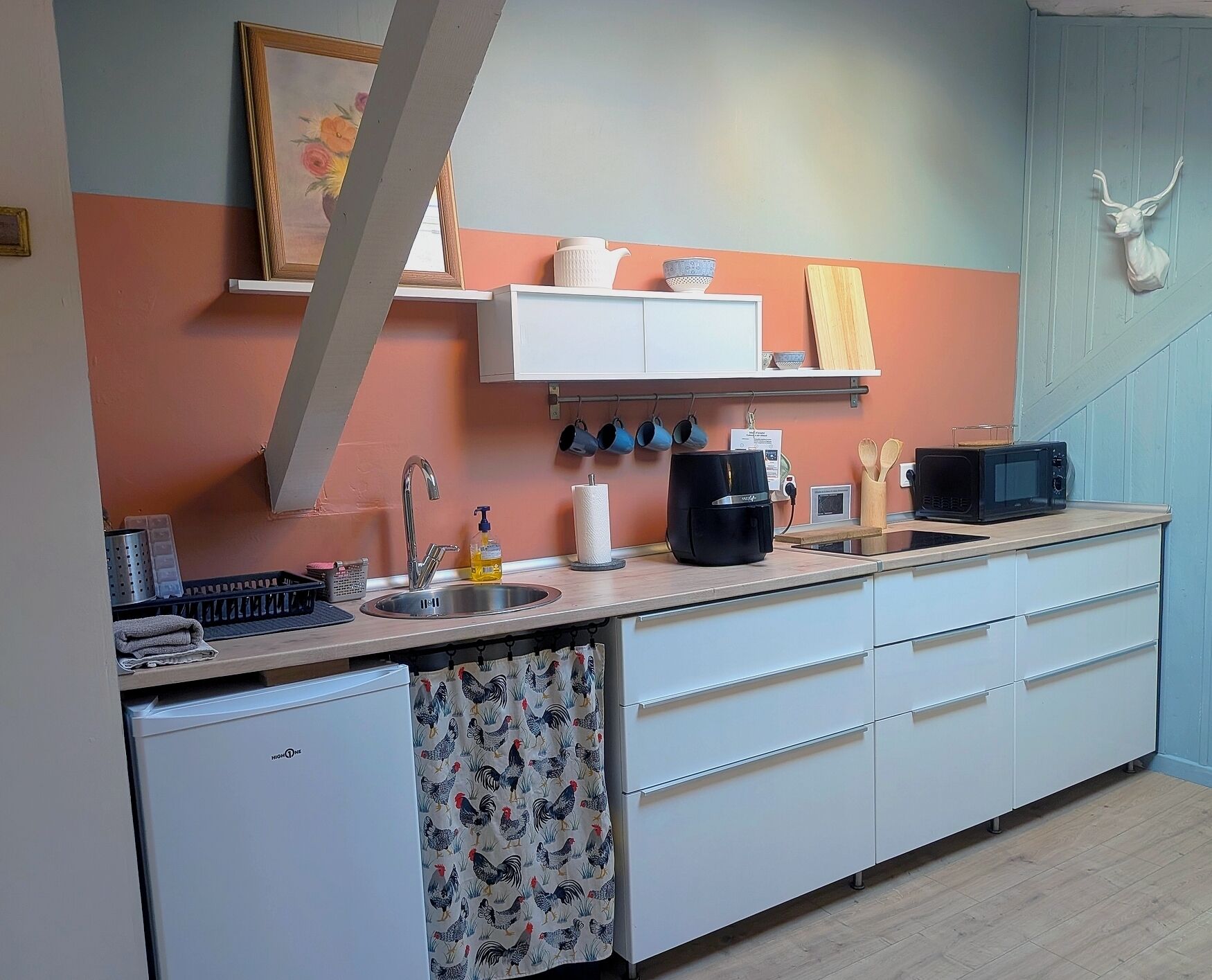 A compact kitchen with a sink, a microwave, and a small refrigerator. There are cabinets and a countertop with various kitchen items.