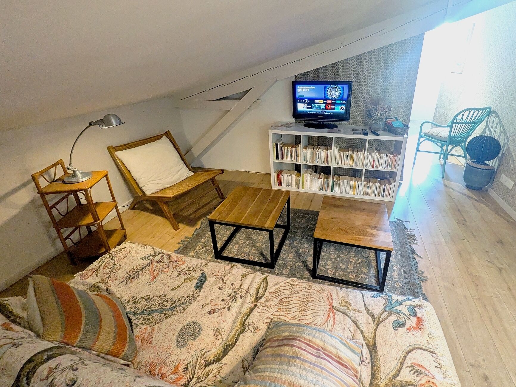 Una sala de estar estilo loft acogedora, con techo inclinado, un sofá de madera, una mesita pequeña, una silla, una estantería y un televisor montado en la pared.
