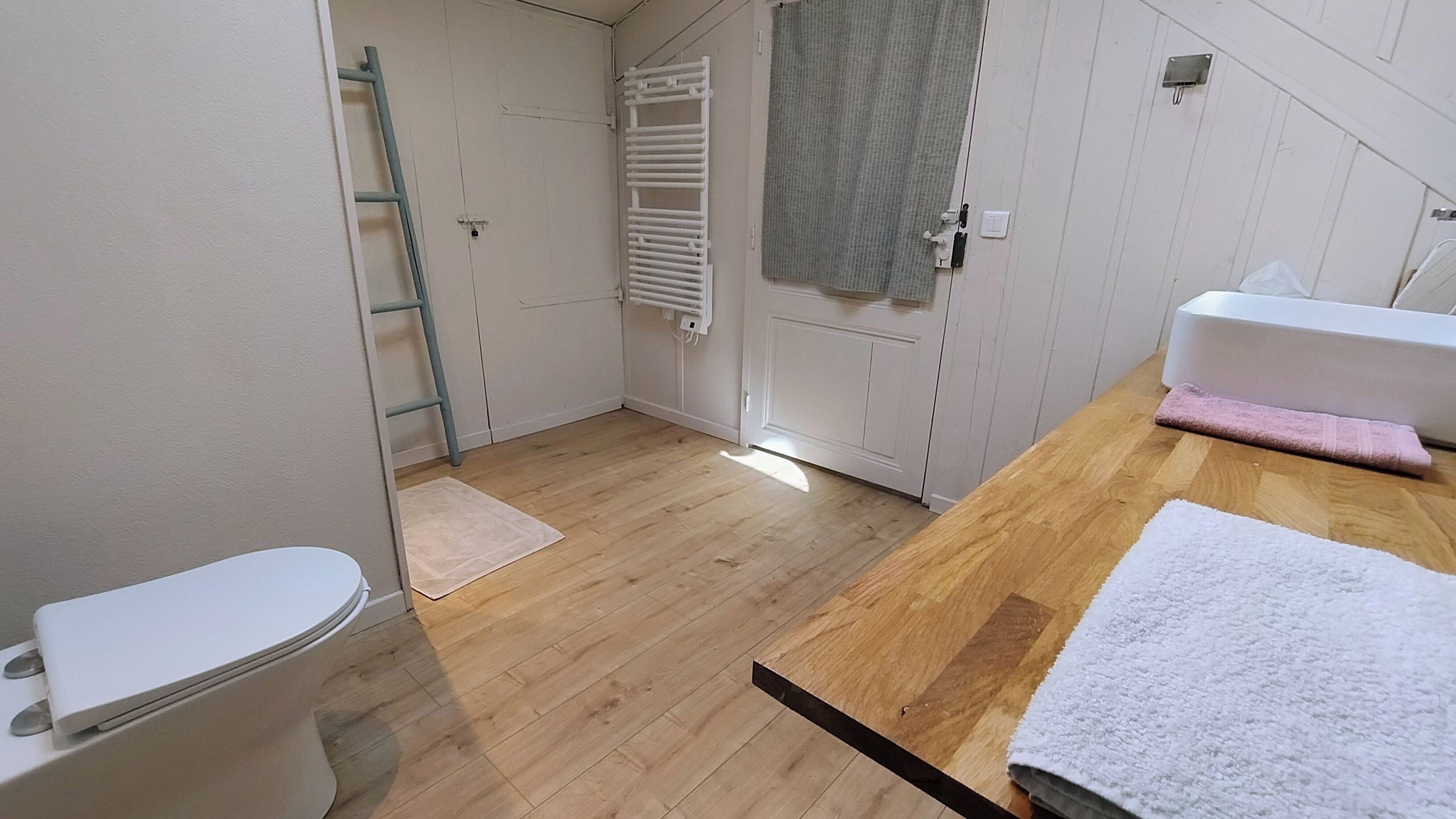 Une petite salle de bain propre, équipée de toilettes, d’un meuble-lavabo en bois et d’un porte-serviettes.