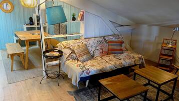 Une chambre mansardée chaleureuse, aménagée avec un canapé, une petite table, une lampe sur pied et une bibliothèque.