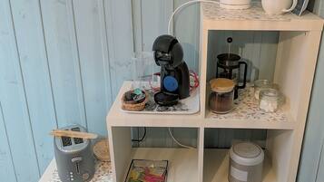Een keuken met een koffiezetapparaat, een waterkoker en diverse keukengerei op planken.