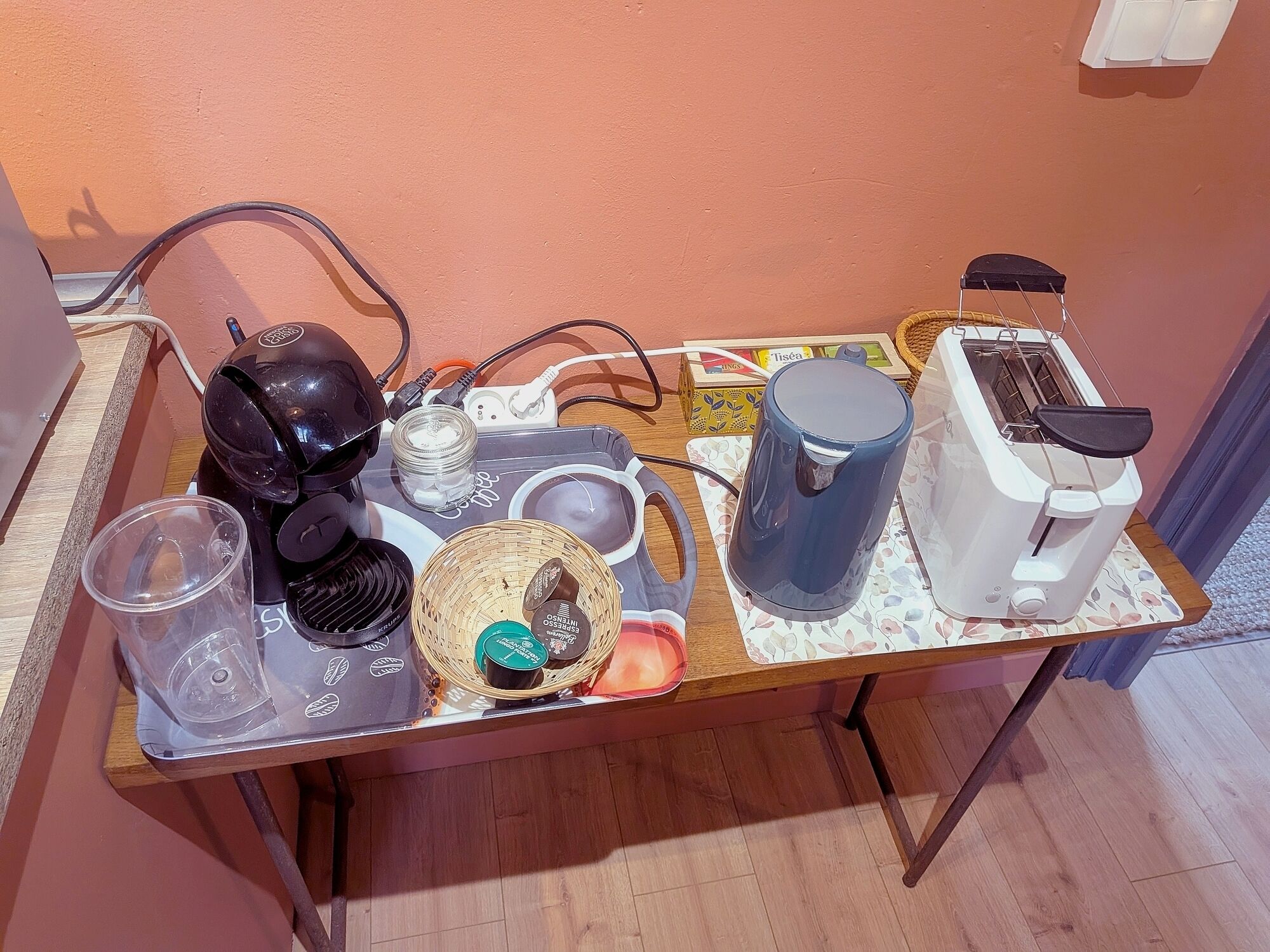 A table with a toaster, a kettle, a coffee maker, a basket, and a cup.
