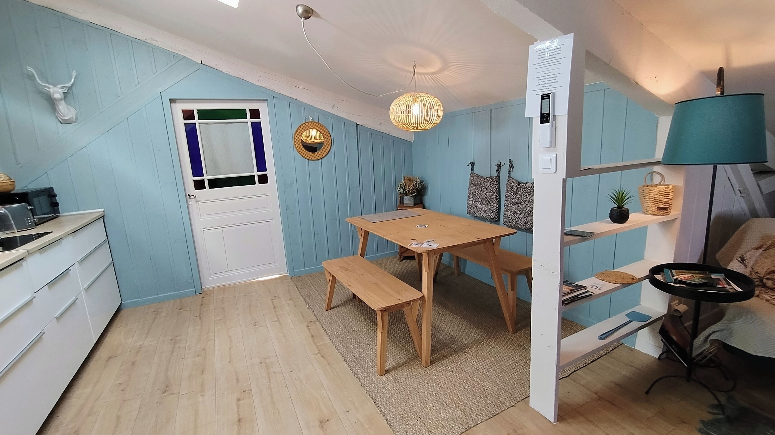 A compact kitchen with a dining area, wooden furniture, a ceiling fan, and a water dispenser.