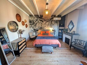 Un dormitorio con una cama grande, una silla, un tocador, un espejo y una chimenea.