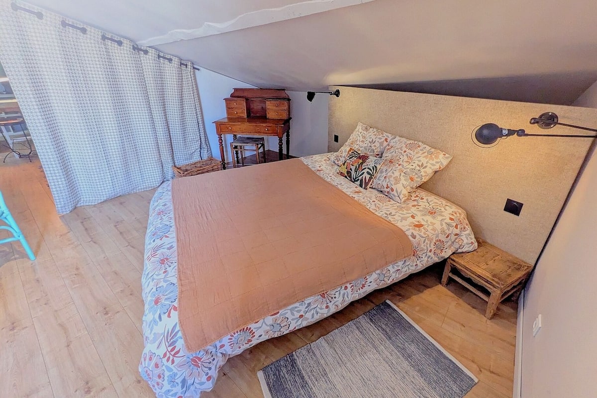 A bedroom with a bed, a nightstand, a chair, a lamp, and a window with curtains.