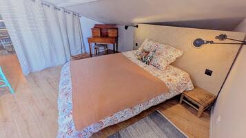 Un dormitorio con una cama, una mesita de noche, una silla, una lámpara y una ventana con cortinas.