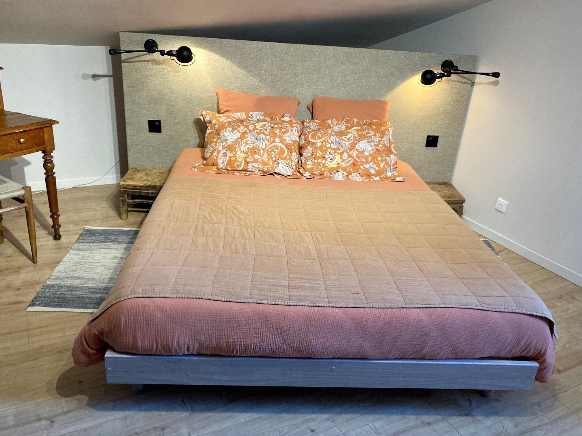 A bedroom with a bed, two bedside lamps, a wooden nightstand, and a small table.
