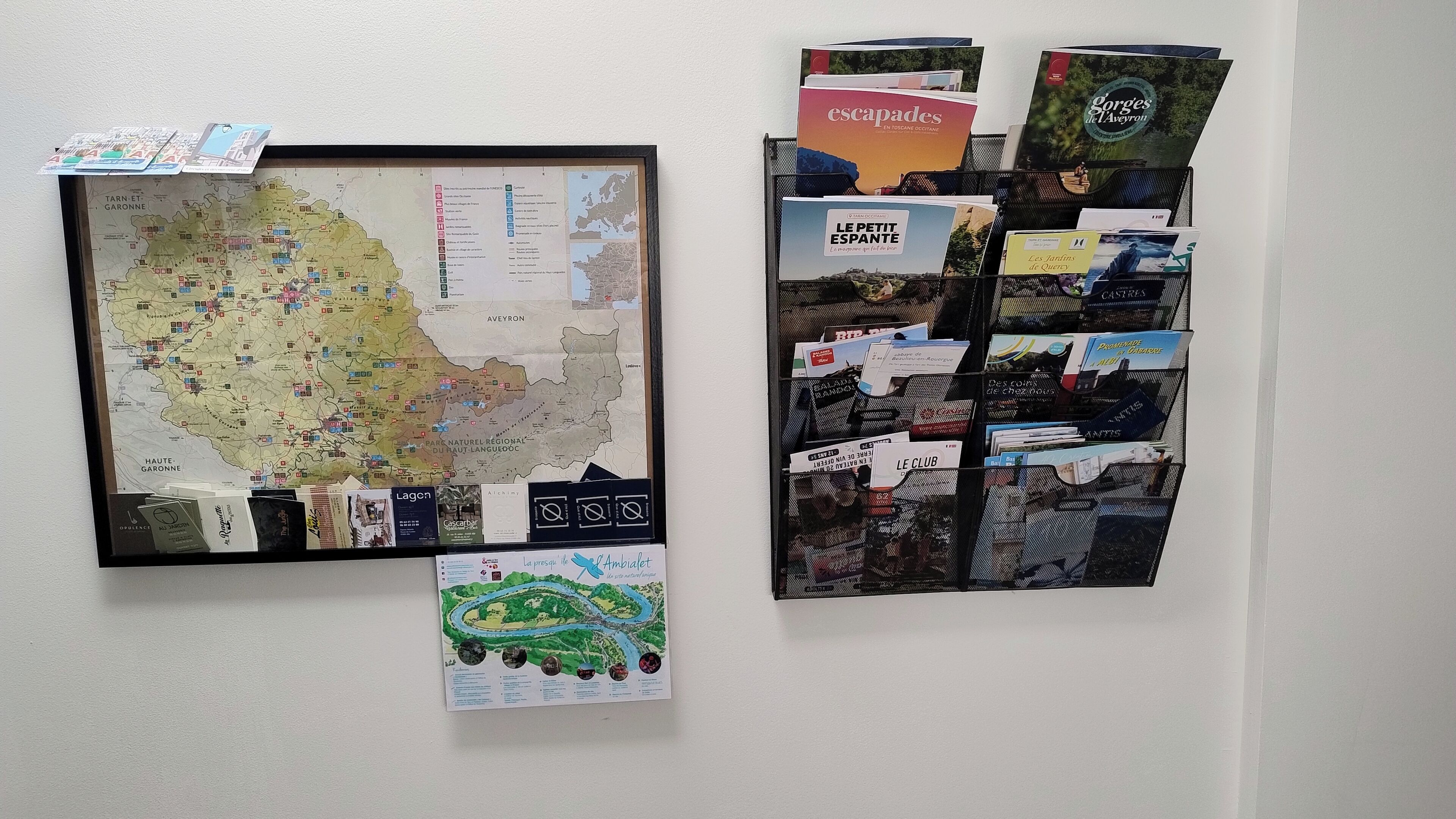 Una pared con un mapa enmarcado y un tablón de anuncios con varios folletos y cuadernillos.