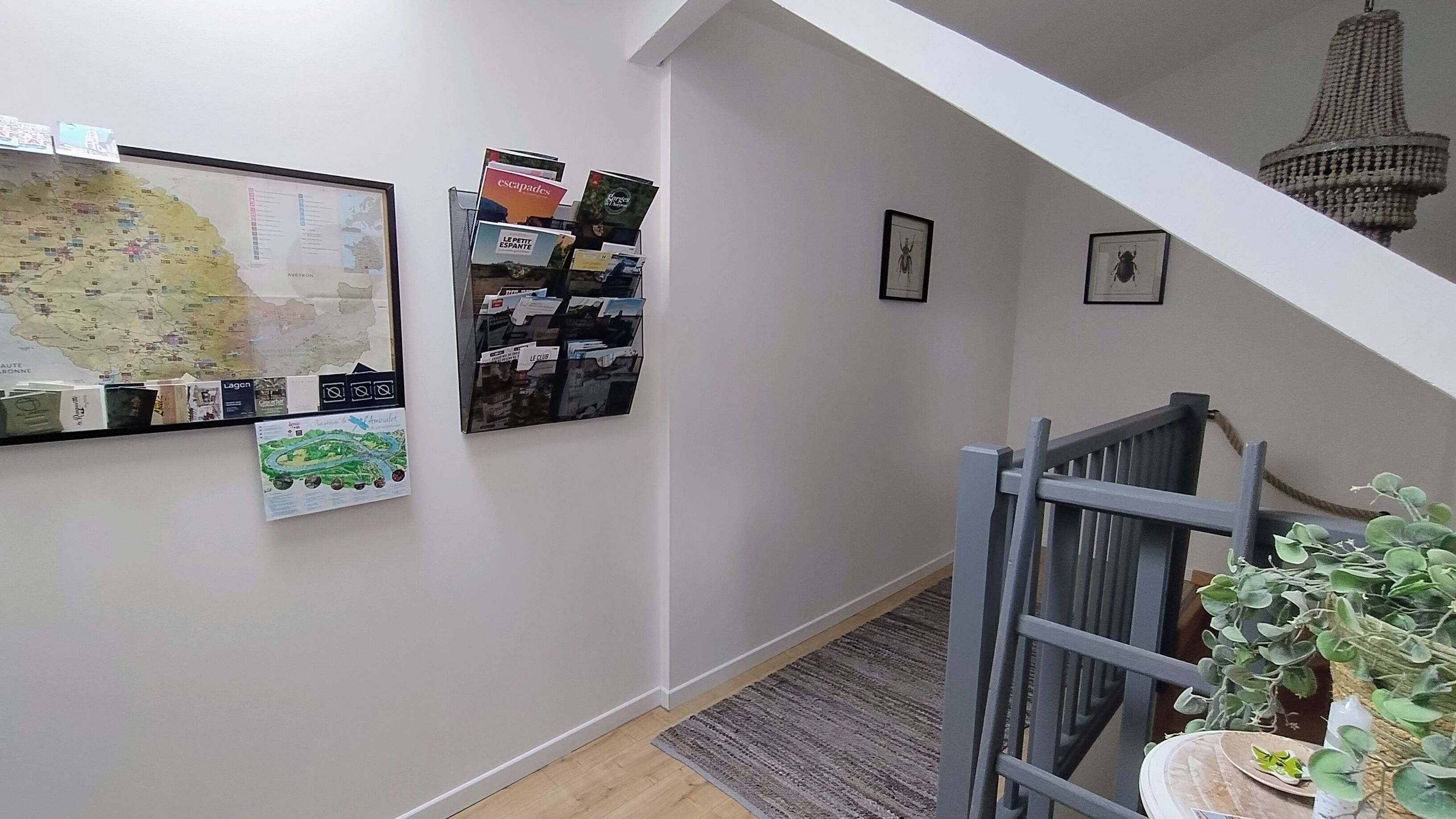 Un couloir avec une carte, un présentoir de cartes postales et des tableaux encadrés accrochés au mur.