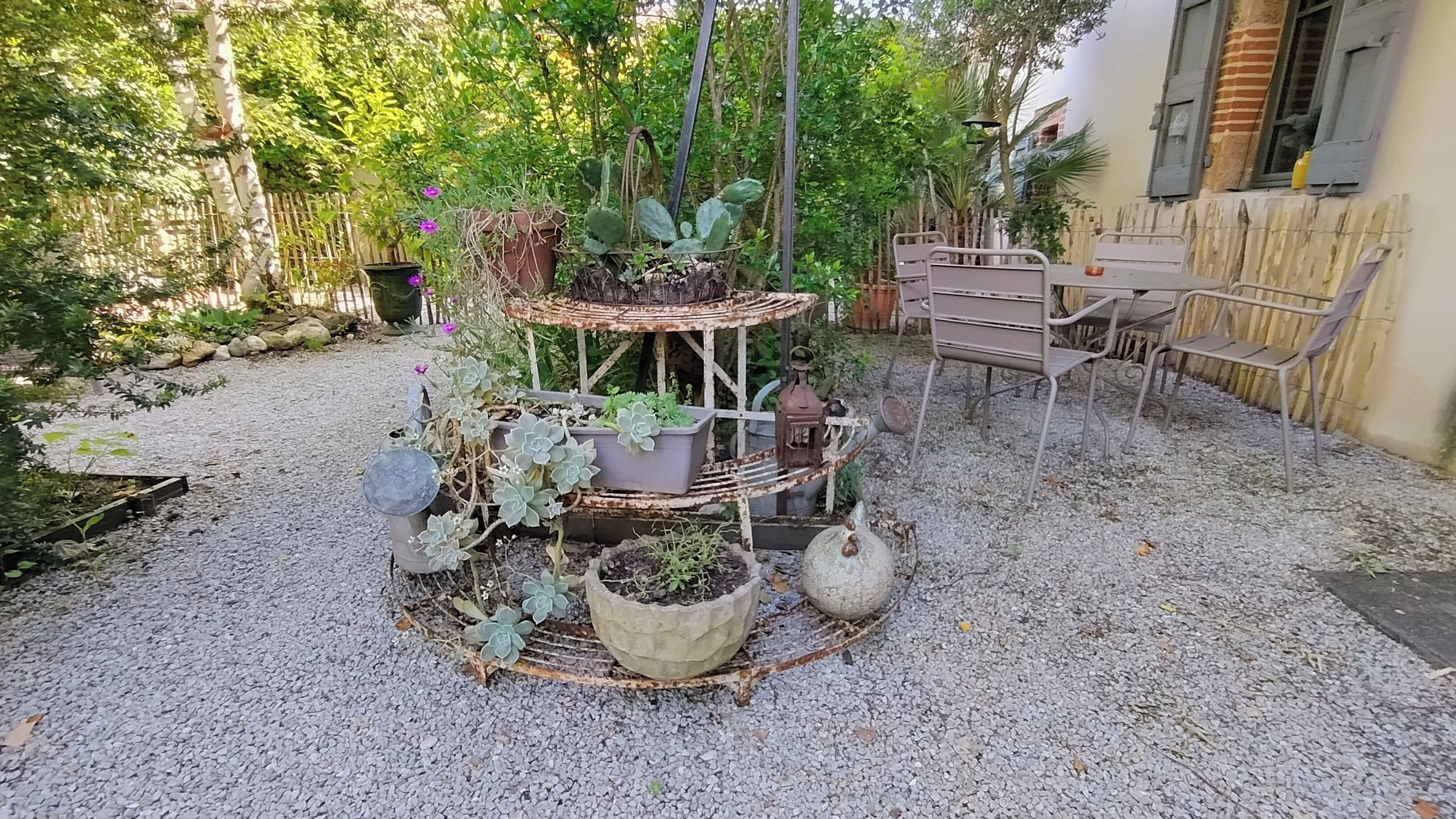 A garden with a multi-tiered planter structure, surrounded by gravel, featuring various potted plants and a rustic metal chair.