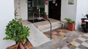 A building entrance with a checkered floor, potted plants, a staircase, and a black door.