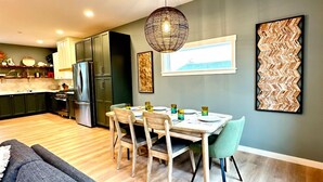 A modern kitchen with dark cabinets, a dining area with a table and chairs, and a grey sofa in the living room. - After Dune Delight is a newly built waterfront escape with peaceful canal views—designed for slow mornings, cozy evenings, and effortless coastal living. (Ocean Shores)