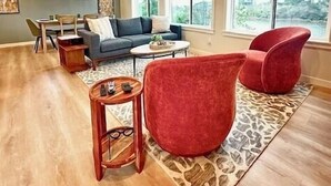 A spacious living room with a sofa, red chairs, a coffee table, and a dining area with a table and chairs. - After Dune Delight is a newly built waterfront escape with peaceful canal views—designed for slow mornings, cozy evenings, and effortless coastal living. (Ocean Shores)