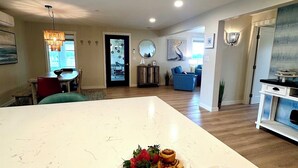 A modern kitchen with a central island featuring a variety of pastries and a dining area with chairs and a table.