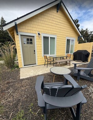 A yellow house with a covered patio, a table with chairs, and a grill.
