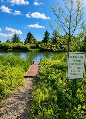 A wooden dock leading to a lake with a sign indicating it is a shared dock for Dune Delight, Dolly Shores, and Yellow Submarine.