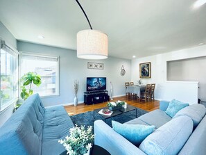A modern living room with a grey sofa set, a coffee table, a TV, and a dining area with a table and chairs. - 804 SanMateo Comfortable 2BR Home/WiFI & Free Parking (San Mateo)