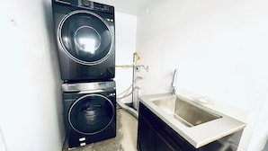 Ein kleiner Waschraum mit nebeneinander gestapelten Waschmaschine und Trockner, einem Waschbecken und einem sichtbaren Wasserrohr.