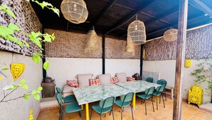 Un espacio comedor al aire libre cubierto, con una mesa y sillas, techo tejido y pared texturizada.