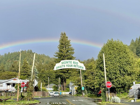 A road sign with a rainbow, houses, and a stop sign.