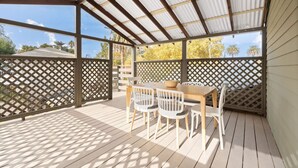 Eine überdachte Terrasse im Freien mit einem Holztisch und -stühlen, umgeben von einem Gitterzaun.