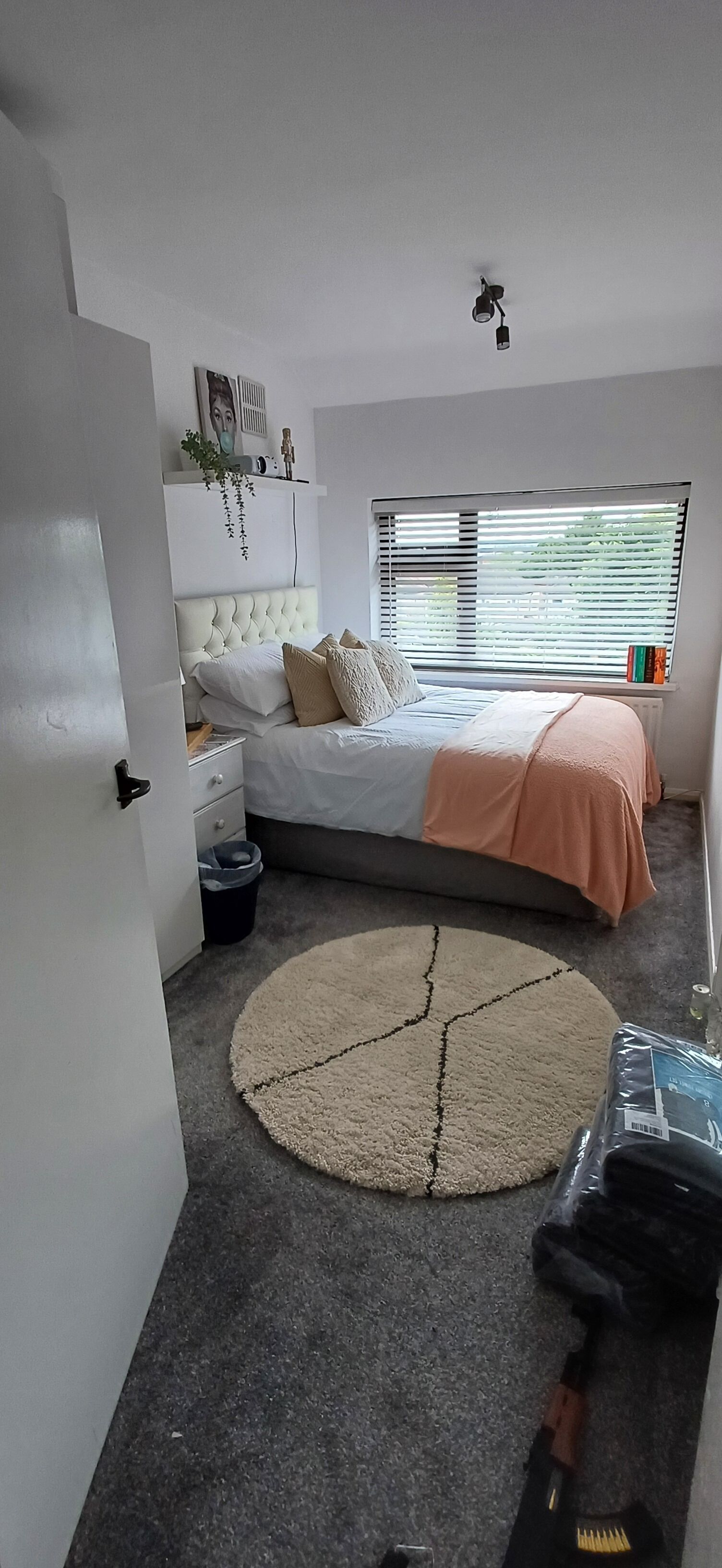 A bedroom with a bed, bedside table, and a window with blinds.