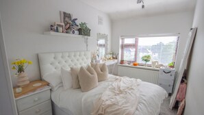 Une chambre à coucher avec un grand lit, des tables de chevet, une commode, une fenêtre avec des stores et un radiateur.