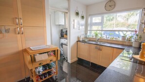 Une cuisine avec des meubles de rangement en bois, un plan de travail noir, un lave-linge et une fenêtre agrémentée de plantes.