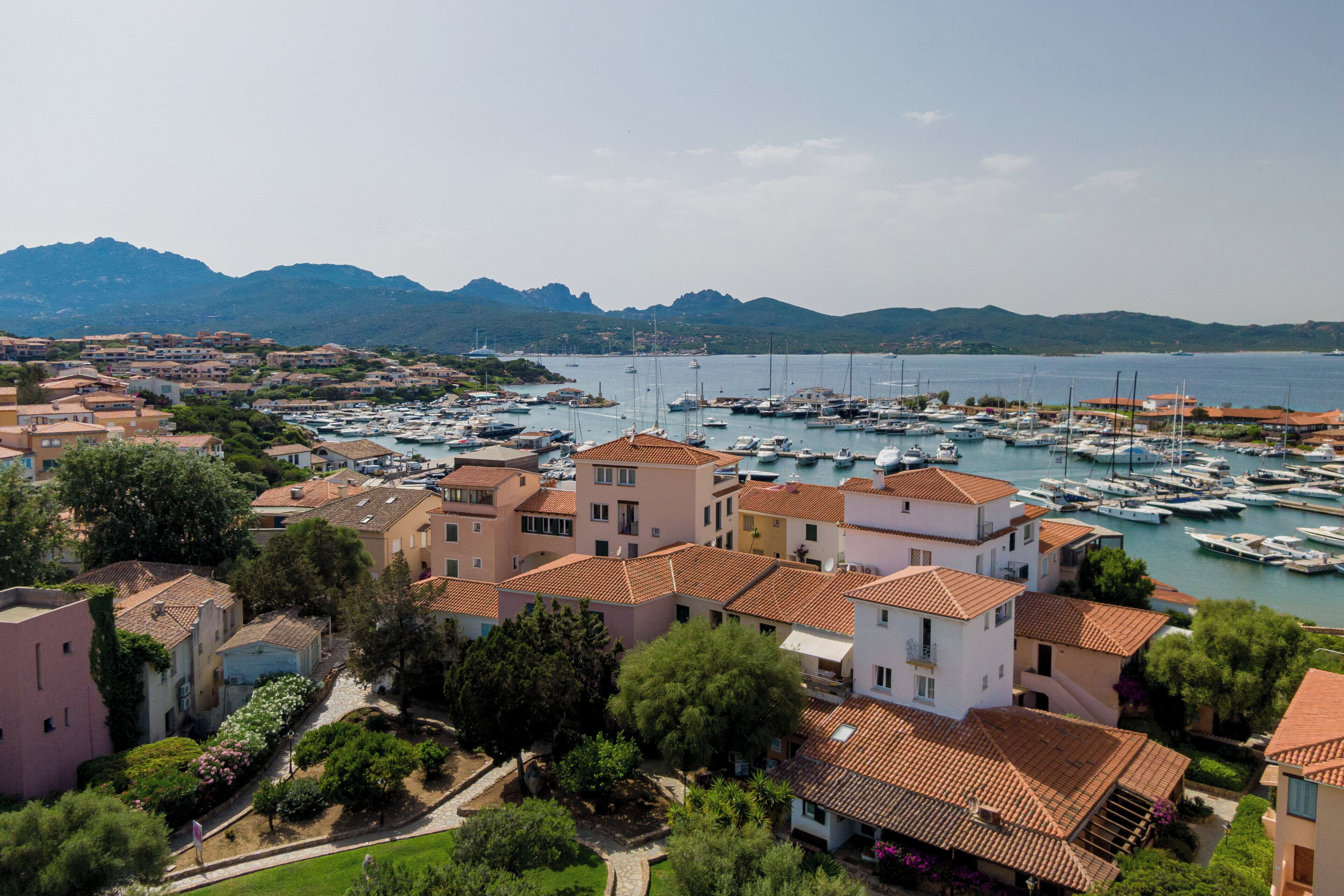 A coastal town with a marina filled with boats, surrounded by residential buildings with red-tiled roofs.