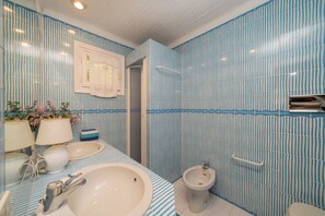 A bathroom with striped blue and white tiles, a sink, a bidet, and a mirror with a towel hanging on it. - Casa Luis by Wonderful Italy (Olbia)