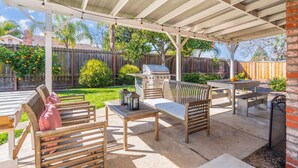 Une terrasse extérieure dotée d’un espace salon couvert, d’un barbecue et d’une table.