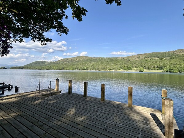 A wooden dock extending into a calm lake with a backdrop of green hills and a clear sky.