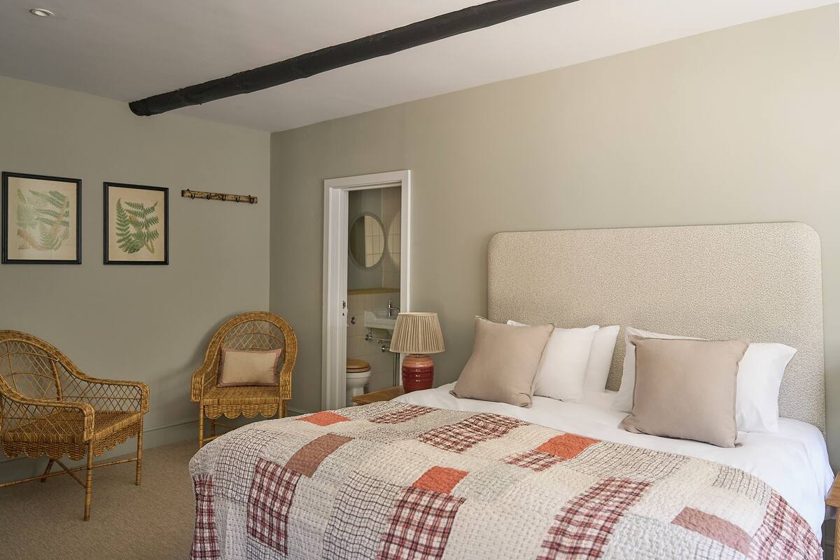 Un dormitorio con una cama grande, dos sillas de mimbre, una puerta de madera y un espejo.
