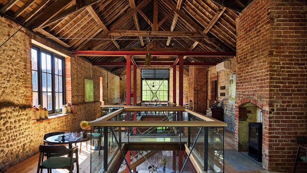 A spacious interior with exposed brick walls, a high wooden ceiling, and a central glass table. - The Maltings (Holt)