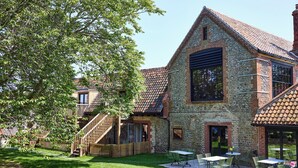 A stone building with a tiled roof, a wooden staircase, and outdoor seating. - The Maltings (Holt)