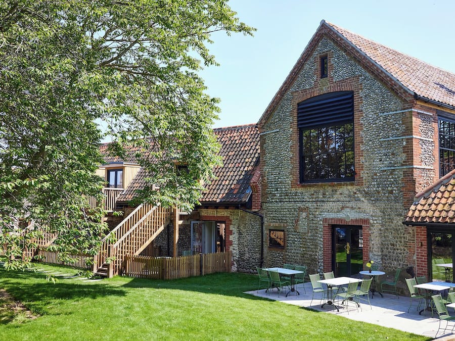 A stone building with a tiled roof, a wooden staircase, and outdoor seating.