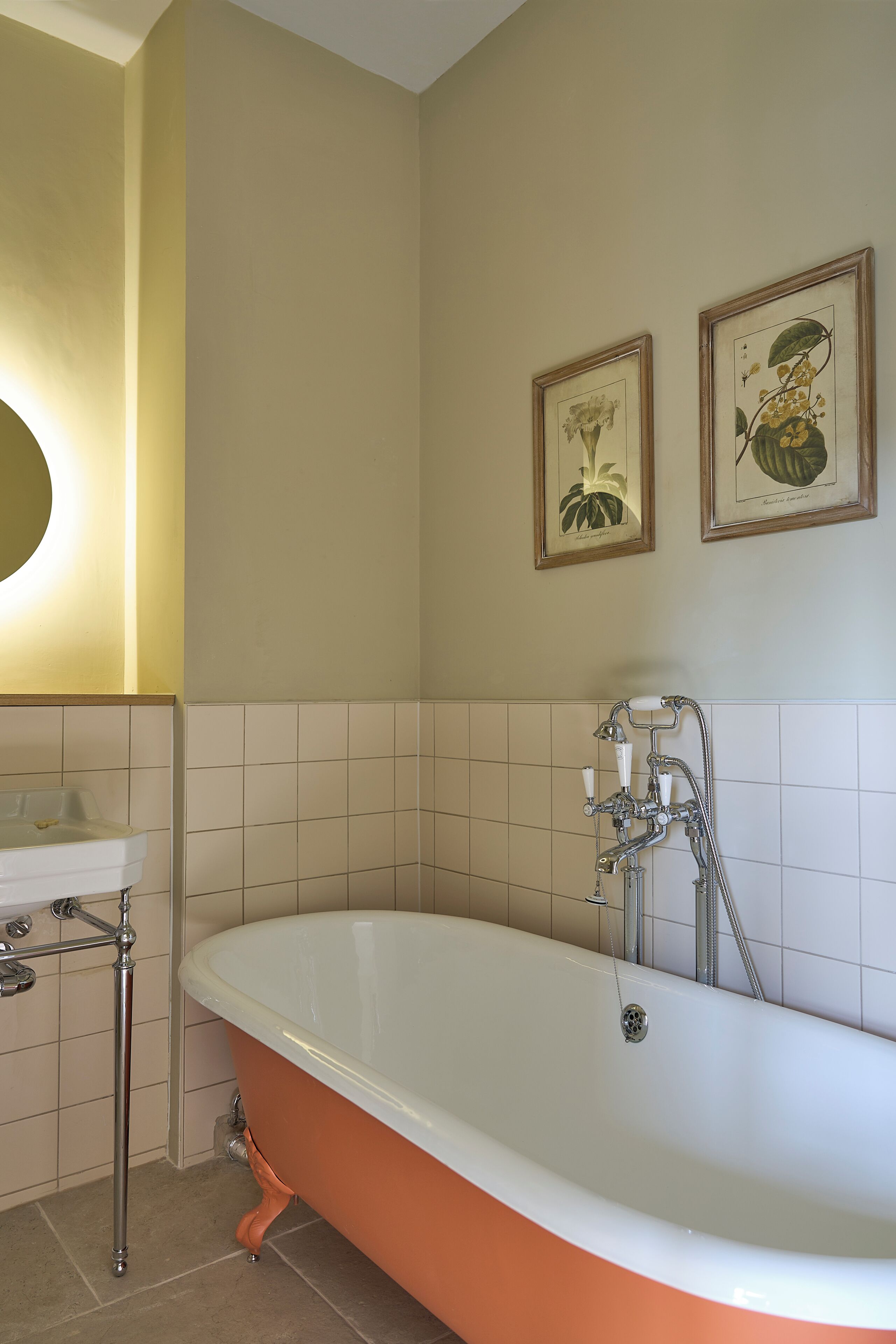 A bathroom with a freestanding bathtub, a sink, and two framed botanical prints on the wall.