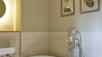 A bathroom with a freestanding bathtub, a sink, and two framed botanical prints on the wall.