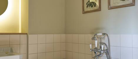 A bathroom with a freestanding bathtub, a sink, and two framed botanical prints on the wall.