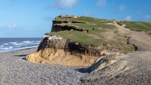 A coastal landscape with a rocky beach, a grassy hill, and a cliff overlooking the sea. - The Maltings (Holt)