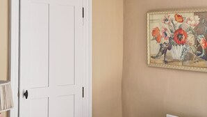 A room with a white door, a beige wall, and a painting of flowers. - The Maltings (Holt)