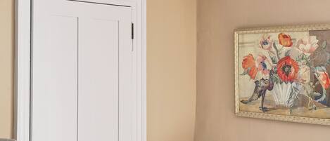 Una habitación con una puerta blanca, una pared color beige y un cuadro de flores.