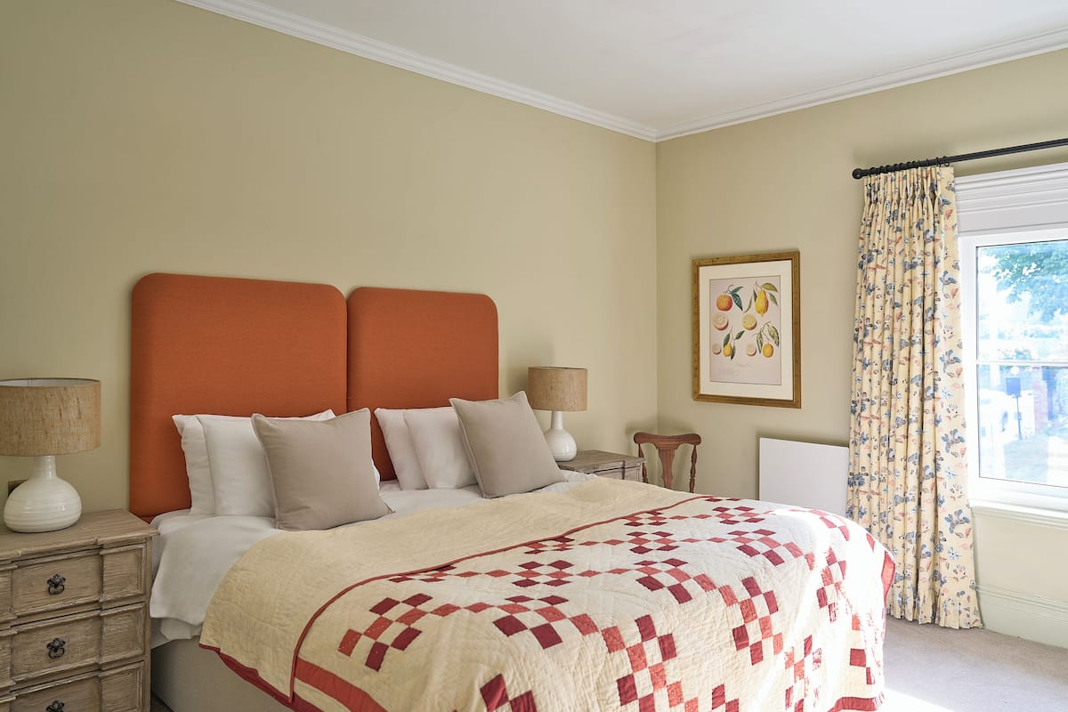 Una cama bien hecha con colcha de cuadros, una mesita de noche con lámpara y un cuadro enmarcado en la pared.