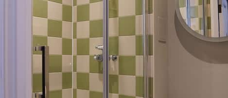 Un baño con ducha envuelta en vidrio, un inodoro y un espejo redondo en la pared.