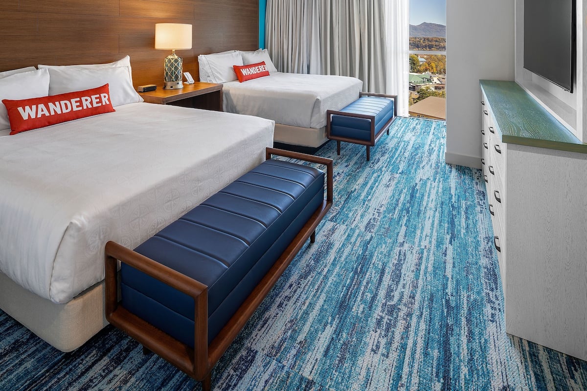 A hotel room with two beds, a desk, a TV, and a view of the outdoors.