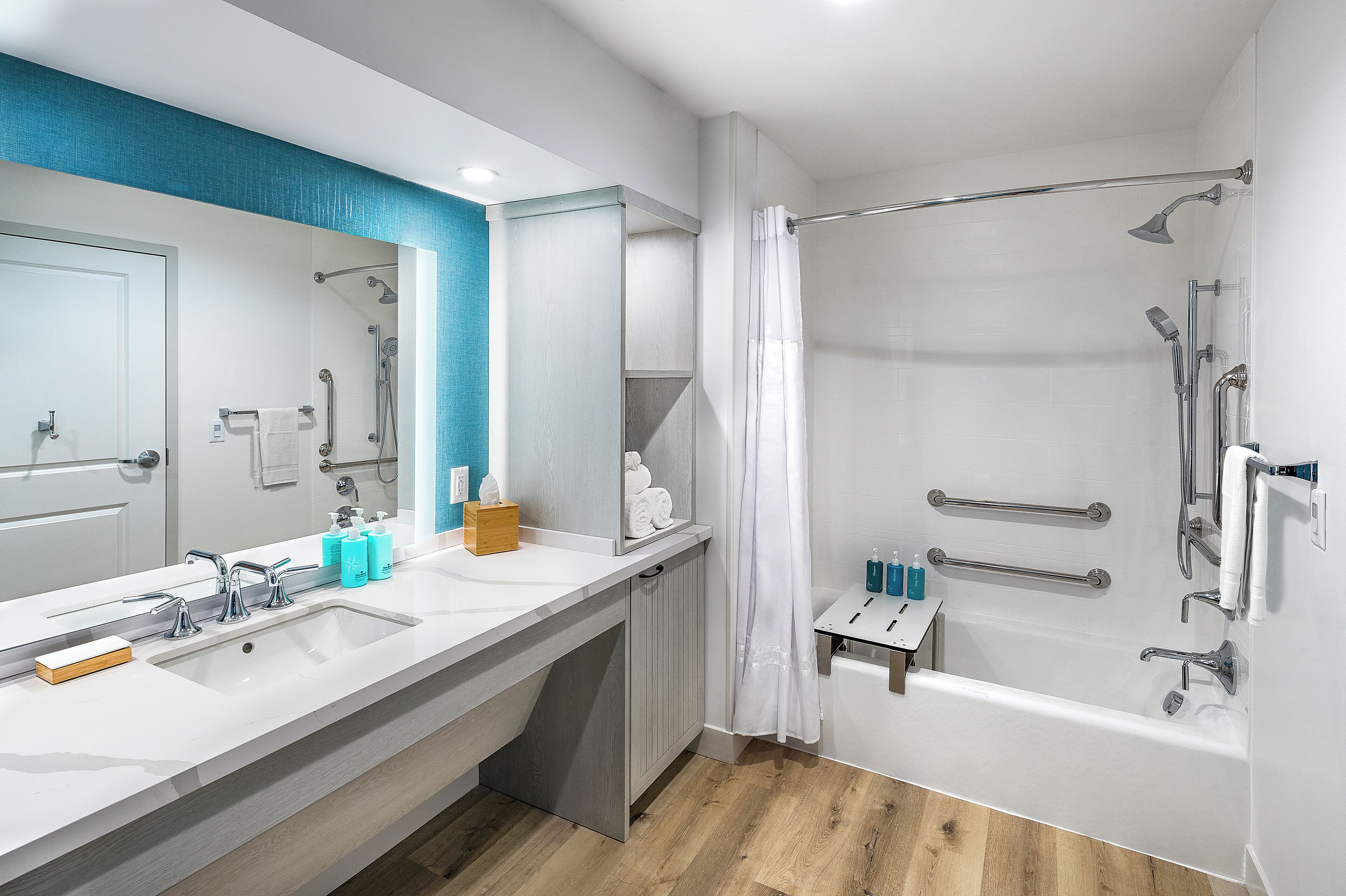 A modern bathroom with a large mirror, dual sinks, a shower with a glass door, and a small vanity with toiletries.